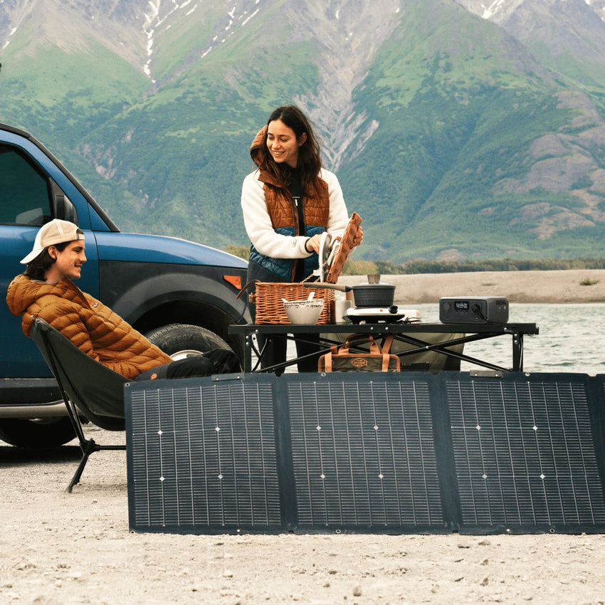 Batterie nomade branché à un panneau solaire en Overland prêt d'une rivière et de montagnes